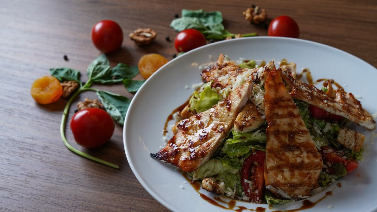 Delicious grilled chicken salad served with fresh tomatoes and walnuts on the side.