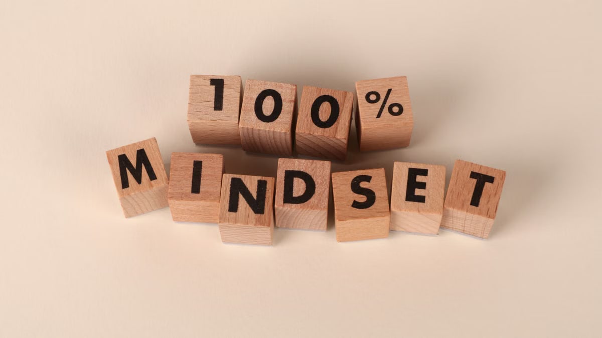 Wooden blocks arranged to spell '100% Mindset' on a neutral beige background, promoting positivity.